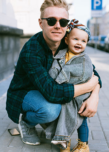 father wearing sunglasses hugging daughter wrapped in a jean jacket