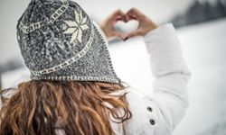 a woman outdoors wearing a wool hat doing "heart hands"