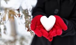 hands wearing wool gloves holding a snow shaped heart