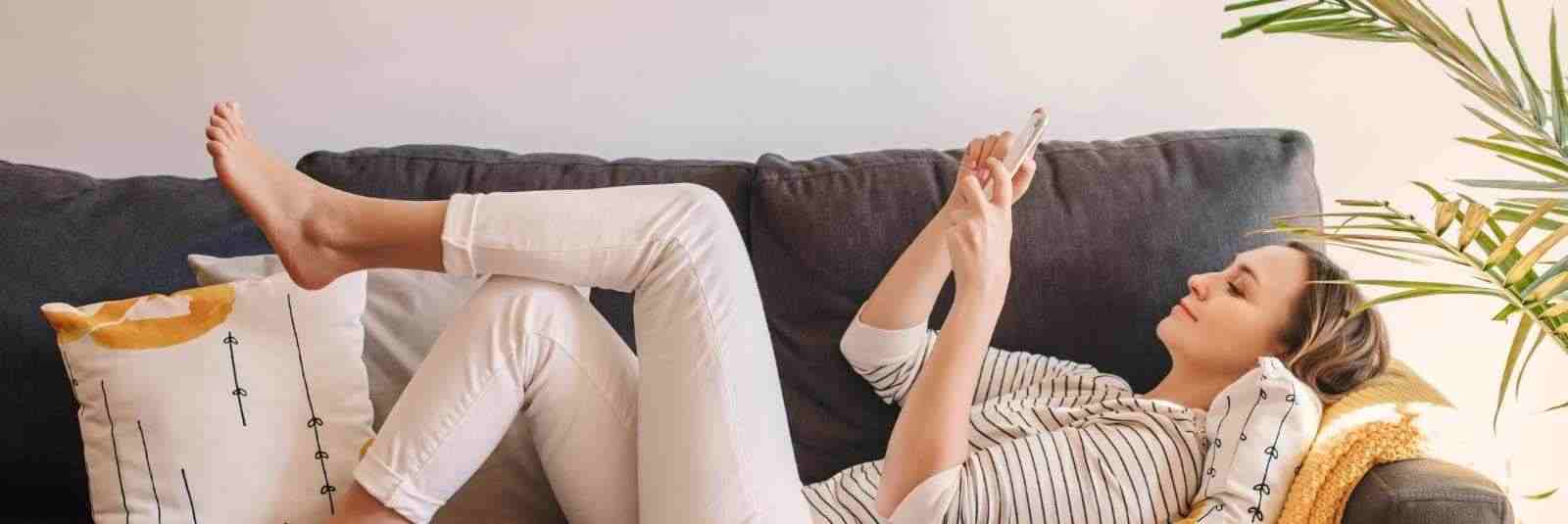 woman laying on couch looking at phone