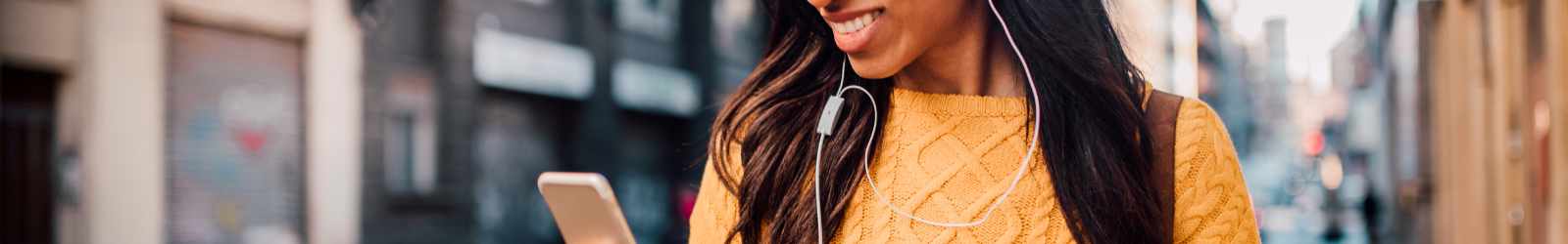 Woman walking and looking at phone with earbuds