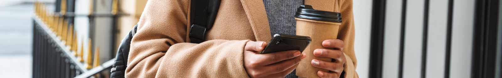 woman walking holding coffee and looking at cell phone