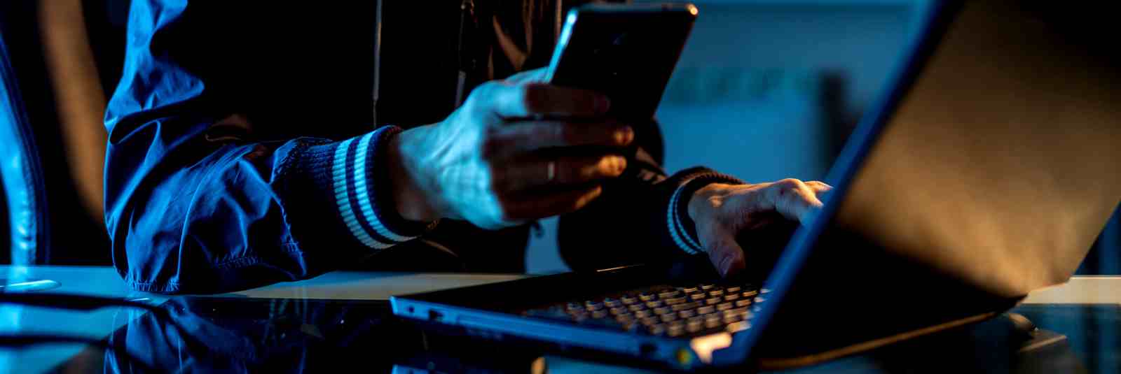 Hacker using computer & phone in the dark